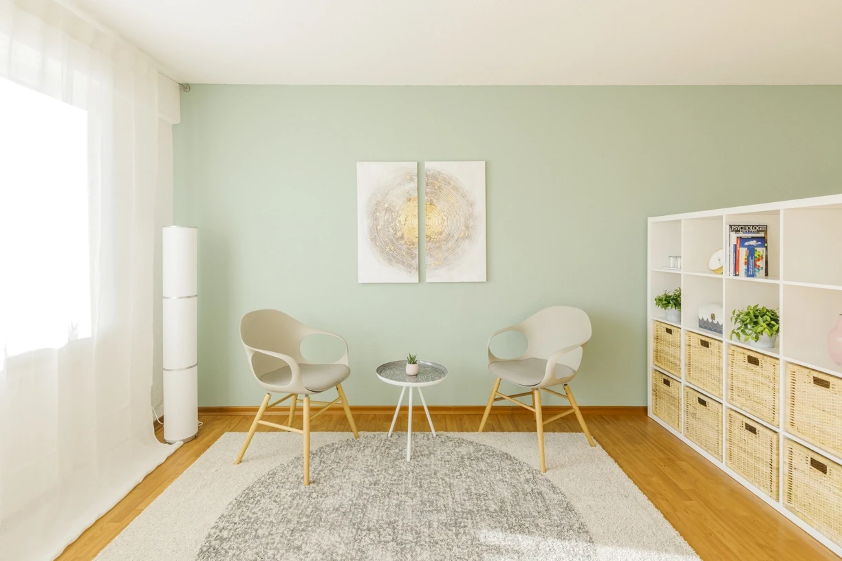 Heller, moderner Raum mit zwei Stühlen, rundem Teppich, Regal und dezenter Dekoration.