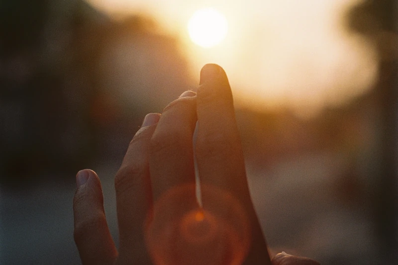 Eine Hand streckt sich bei Sonnenuntergang in warmes Sonnenlicht und erzeugt Lichtreflexe.
